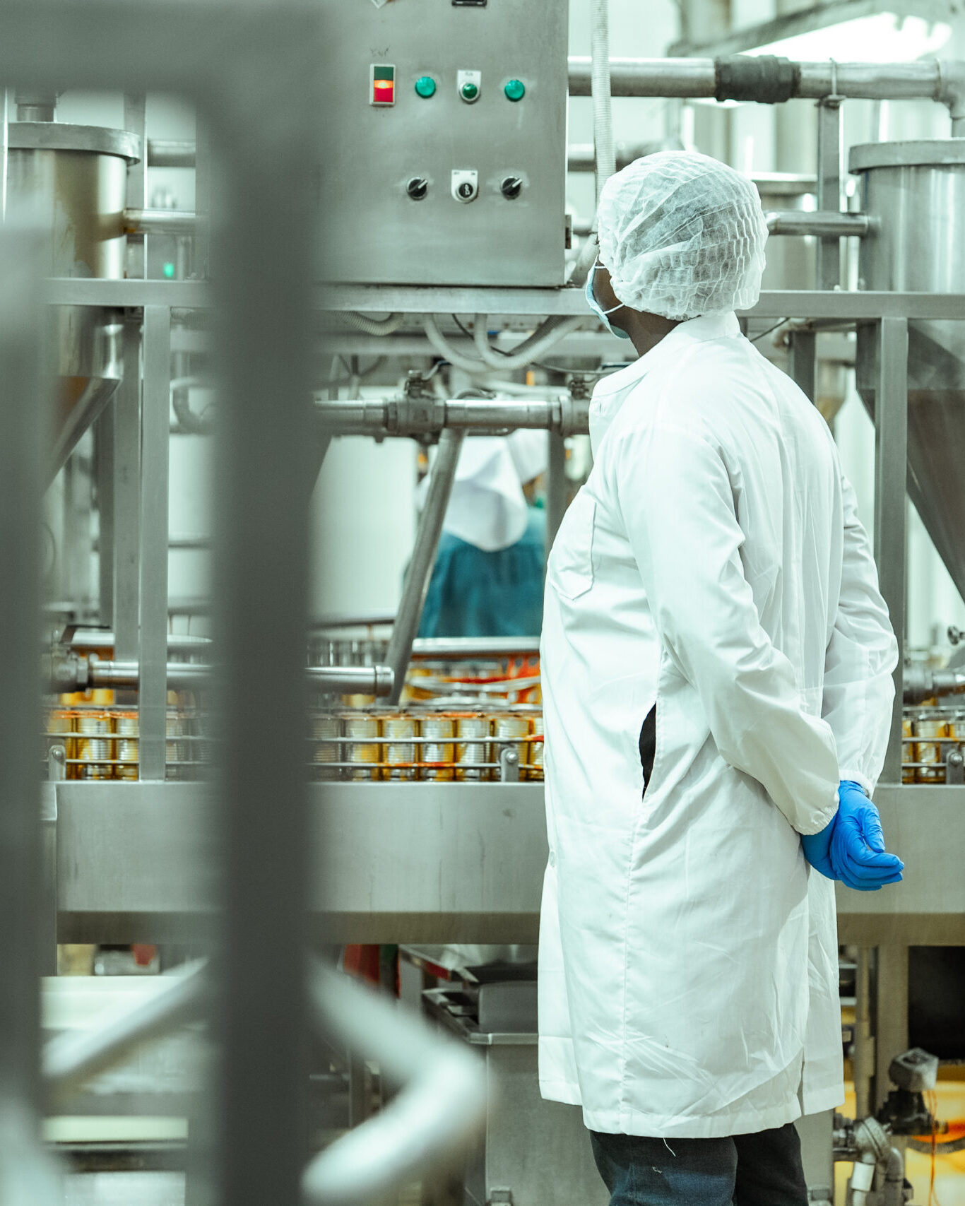 Worker in protective clothing monitoring food production equipment inside a modern manufacturing facility.