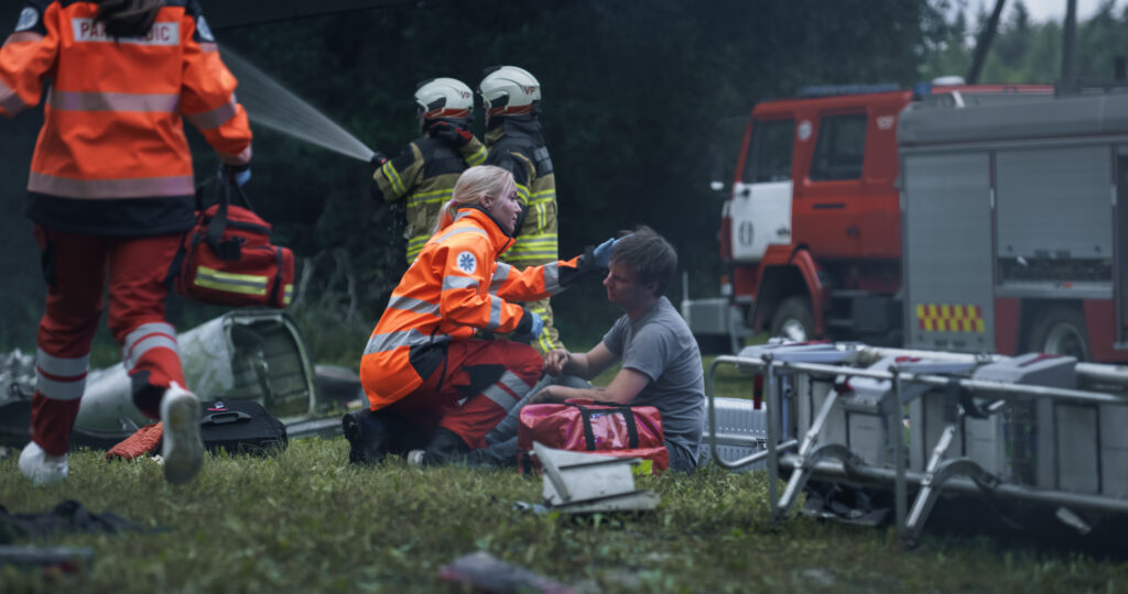 Emergency responders providing medical assistance beside emergency vehicles at an outdoor incident scene.